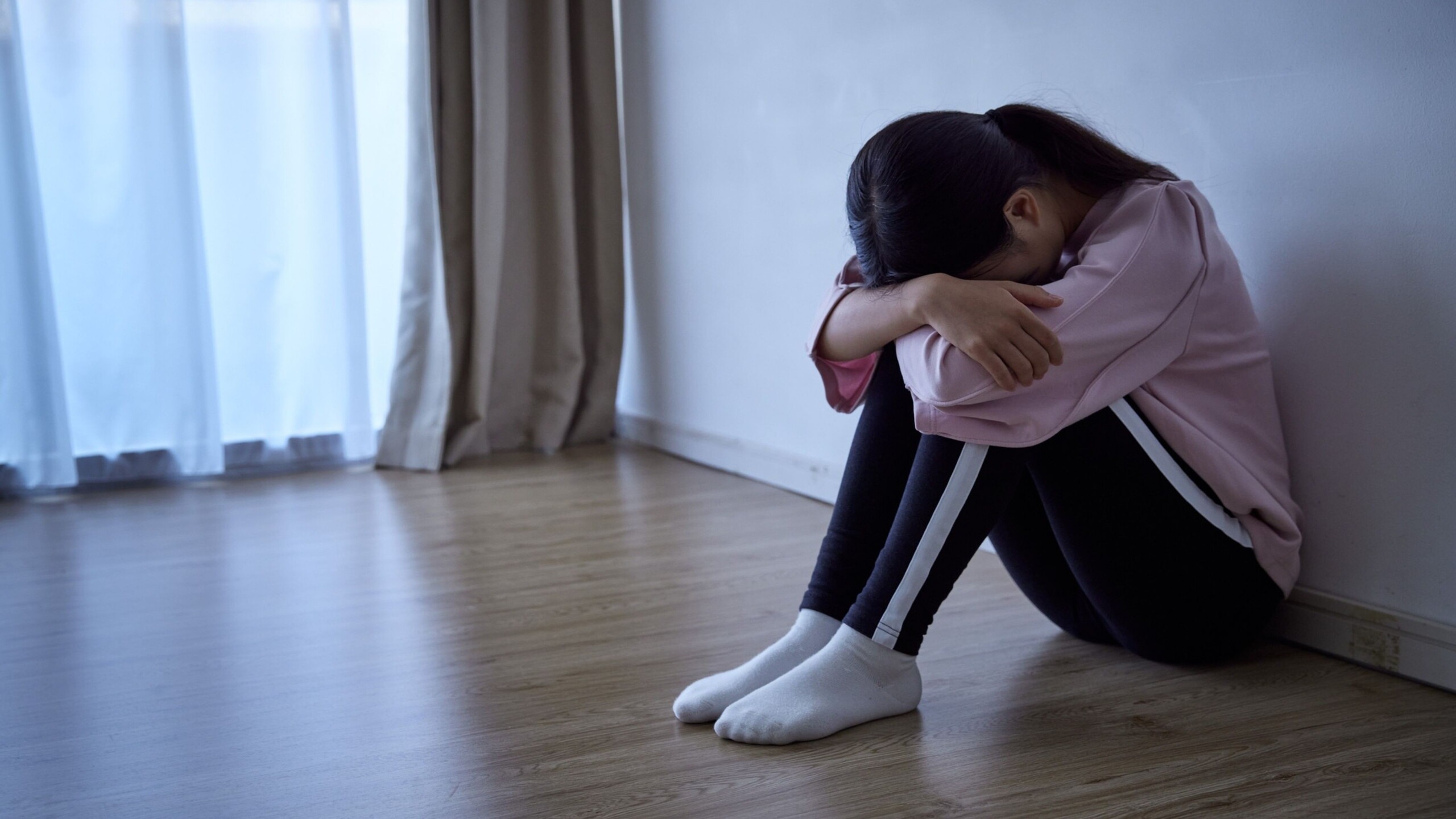 Verdrietig kind zit ineengedoken in een hoek van de kamer